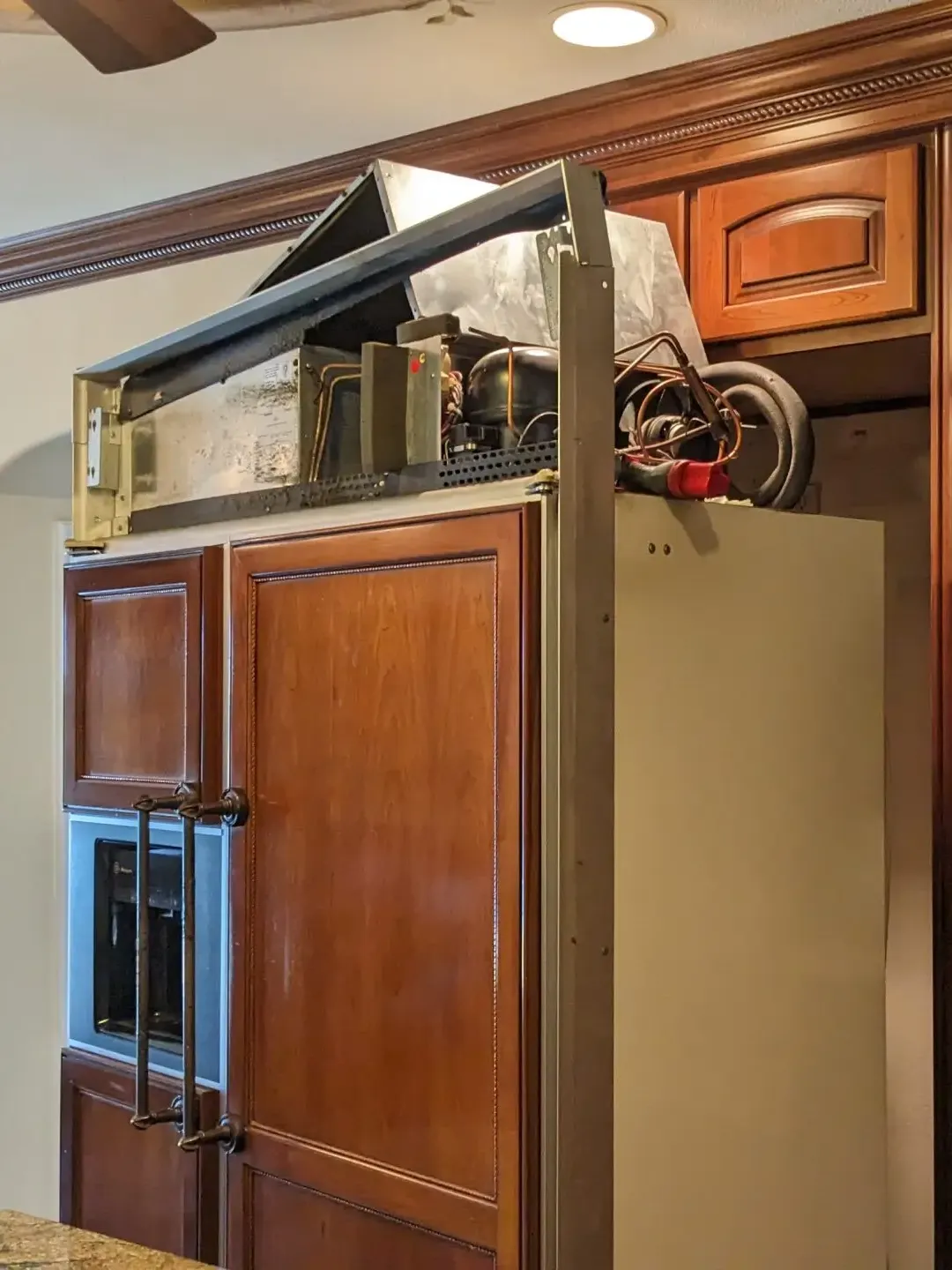 Panel-ready built-in refrigerator in a cherry-wood kitchen with the compressor compartment pulled out for service
